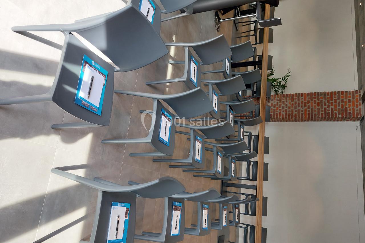 Chaises grises alignées dans une salle lumineuse, chacune portant un document posé sur l'assise.