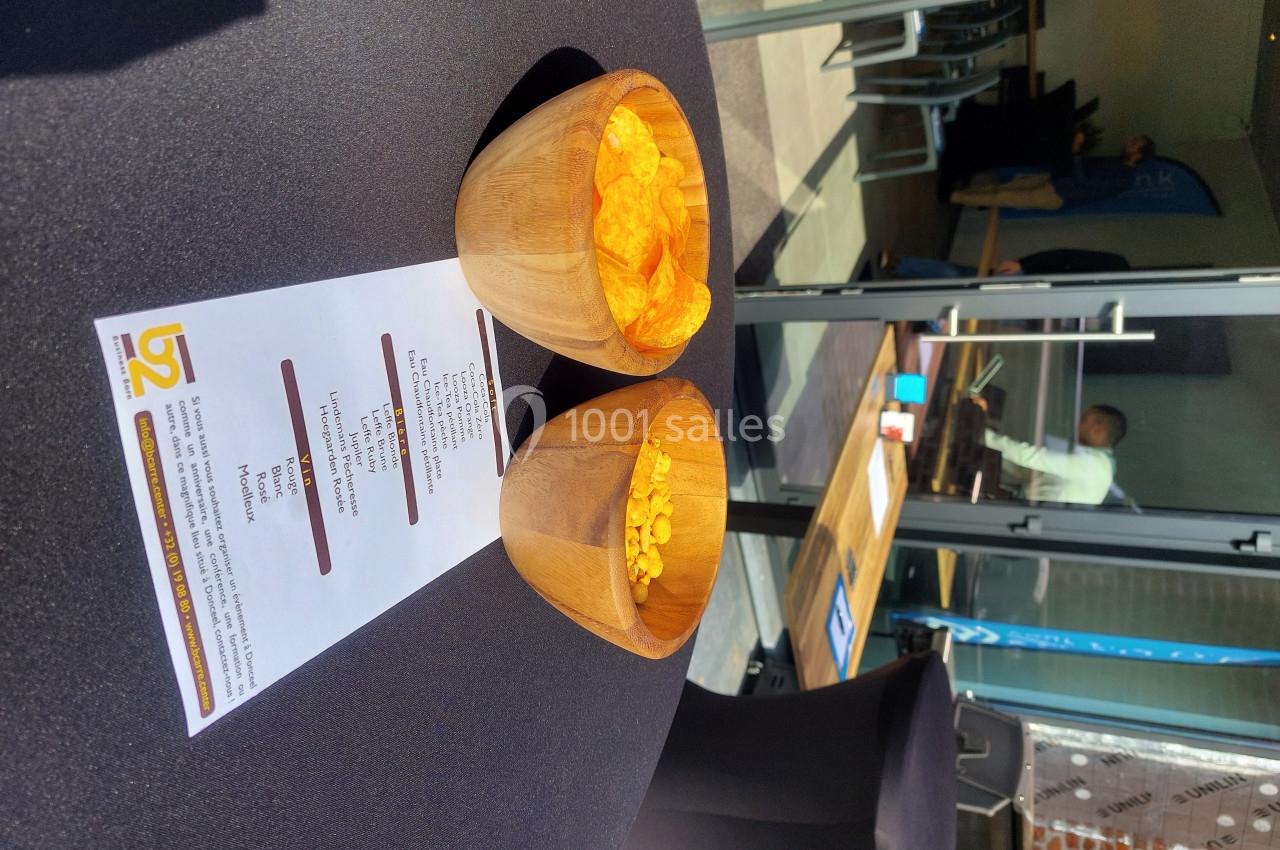 Deux bols en bois contenant des chips posés sur une table noire avec un menu imprimé, en extérieur près d'une baie vitrée.