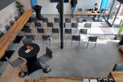 Salle de réunion moderne avec chaises disposées en rangées, tables hautes et grandes baies vitrées laissant entrer la…