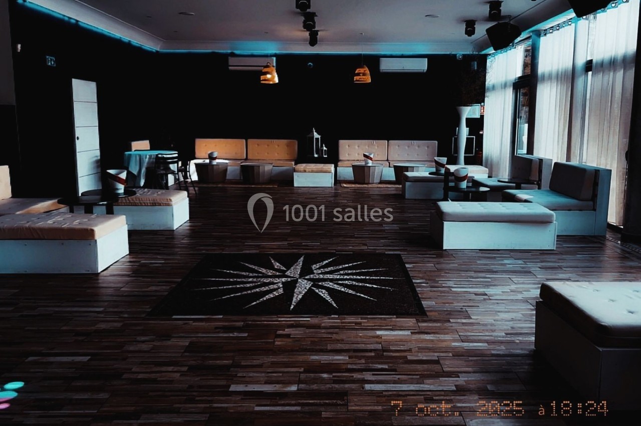 Salle vide avec parquet sombre, banquettes blanches, tables basses et éclairage tamisé.