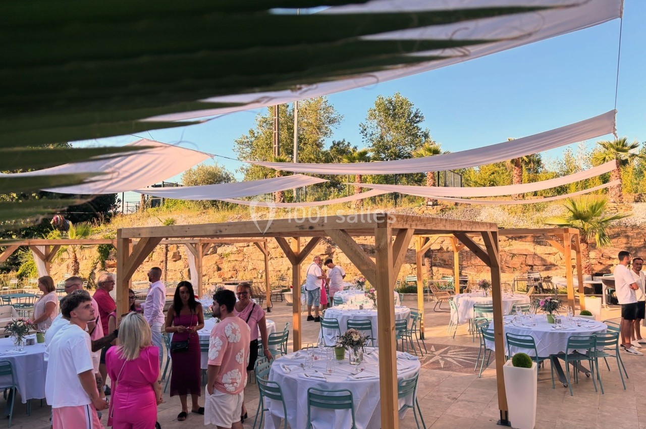 Personnes rassemblées dans un espace extérieur décoré avec des tables dressées et des voiles suspendues.