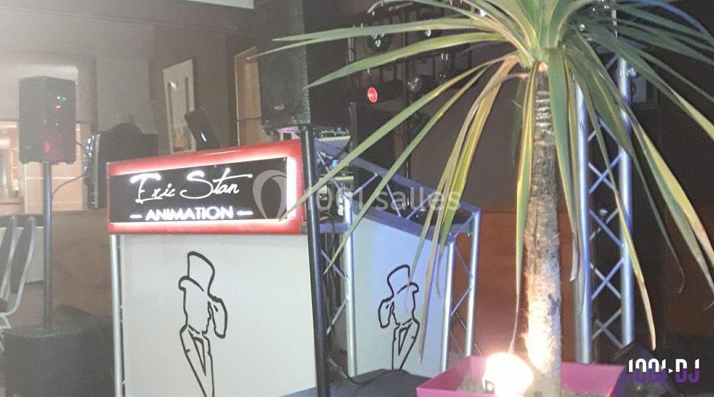 Console de DJ éclairée avec l'inscription ’Éric Stan Animation’, entourée d'équipements audio et d'une plante décorative.