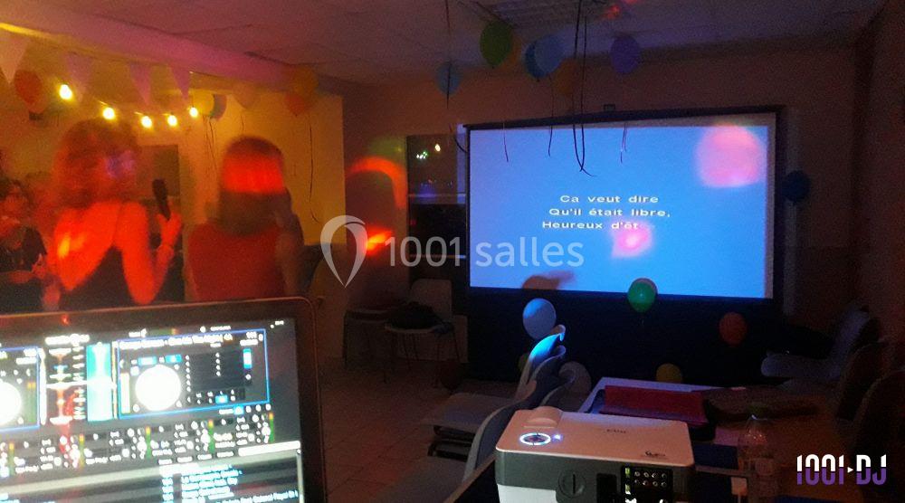 Des personnes chantent devant un écran affichant des paroles de karaoké dans une salle décorée de guirlandes et lumières…