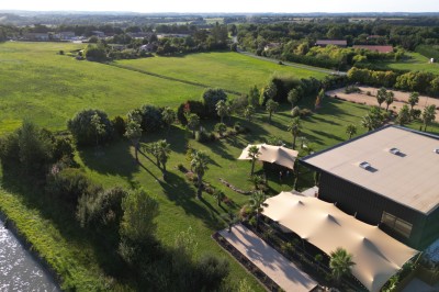 Vue aérienne d'un espace vert avec un bâtiment moderne, des arbres, des toiles d'ombrage et des champs en arrière-plan.
