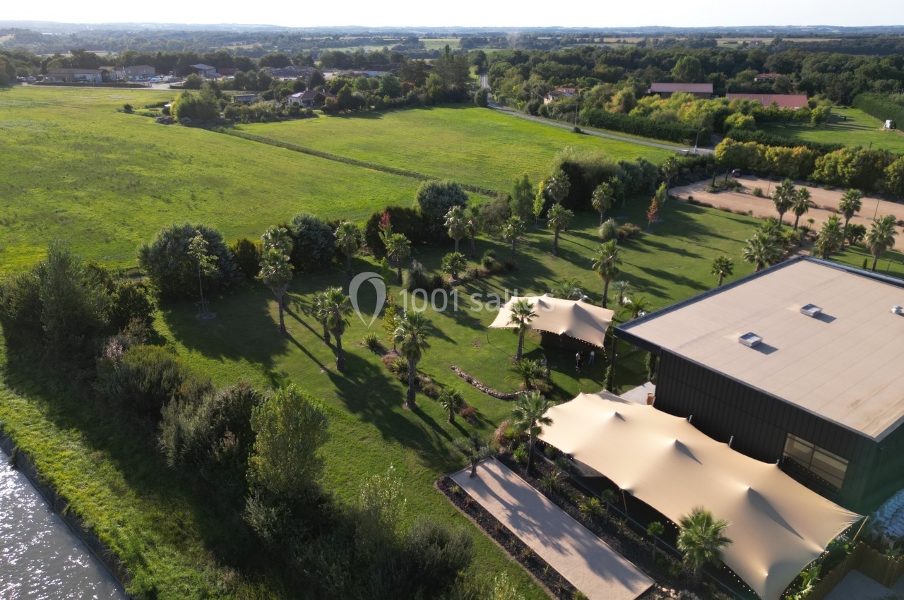 Vue aérienne d'un espace vert avec un bâtiment moderne, des arbres, des toiles d'ombrage et des champs en arrière-plan.