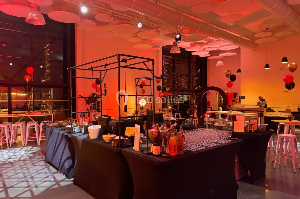 Salle décorée pour un événement avec tables, boissons, ballons rouges et noirs, éclairage tamisé.