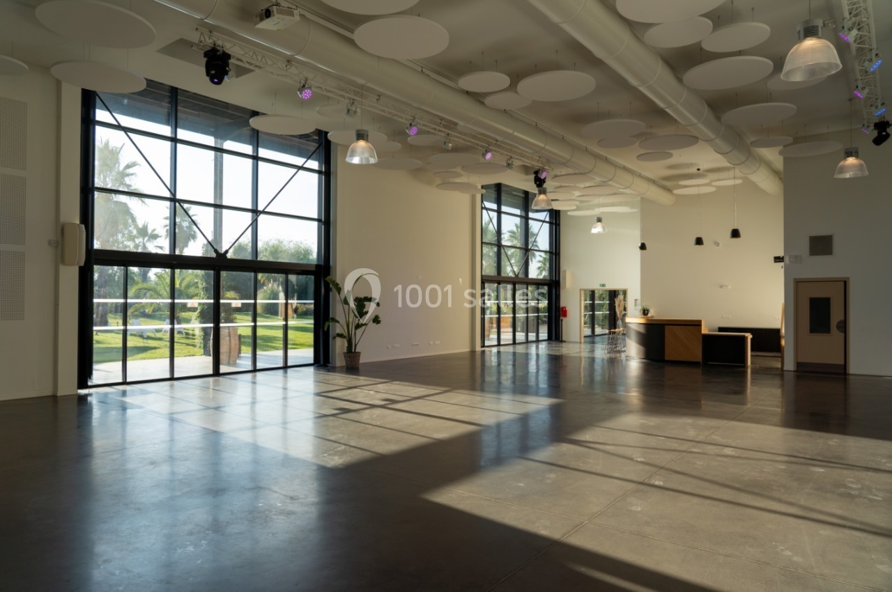 Salle lumineuse avec de grandes baies vitrées, un sol en béton poli, des plantes et un comptoir d'accueil.