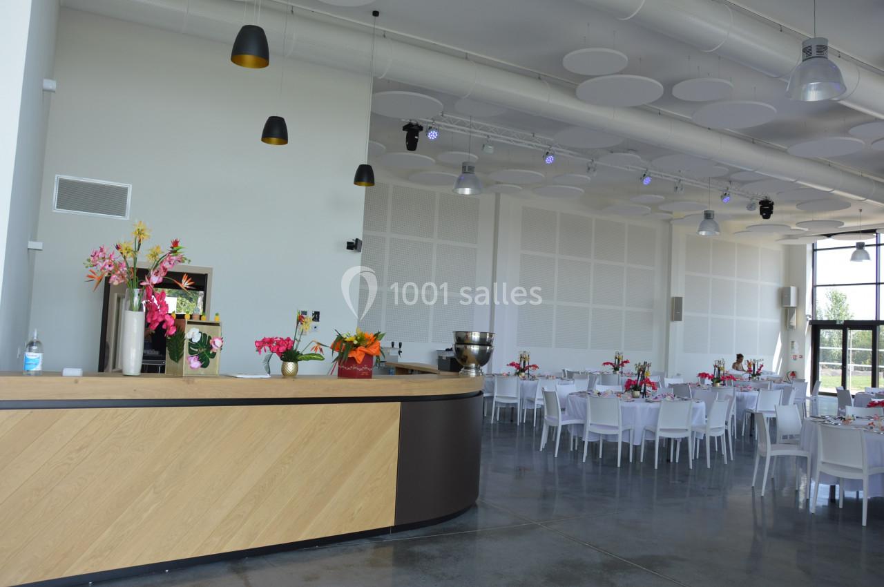 Salle lumineuse avec tables dressées, chaises blanches, décorations florales colorées et un comptoir en bois clair.