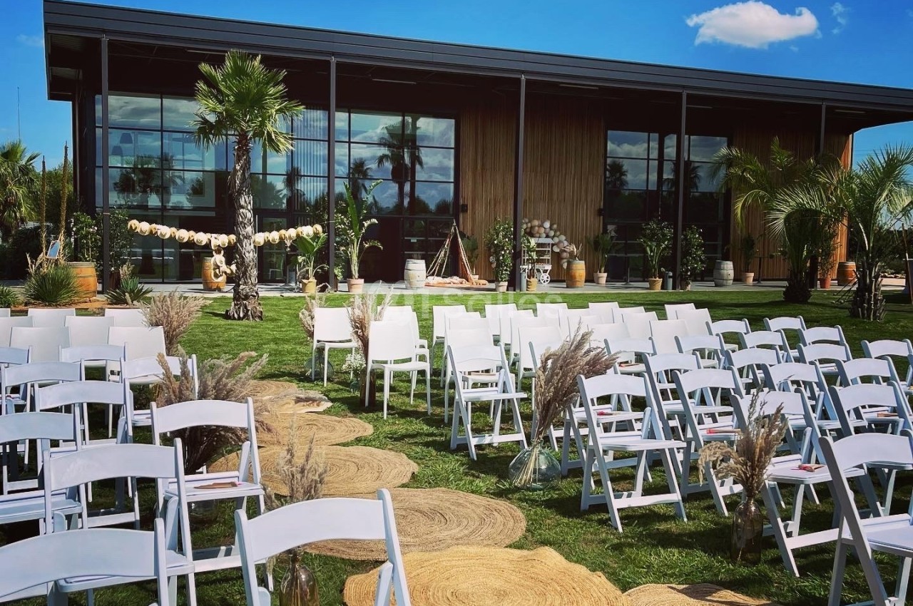 Chaises blanches disposées en rangées sur une pelouse face à un bâtiment moderne, décoré pour un événement en extérieur.