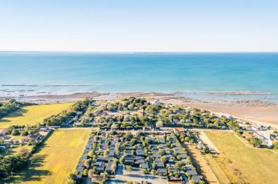 Groupe de personnes rassemblées autour de tables de pique-nique dans un espace extérieur avec des arbres et des parasols.