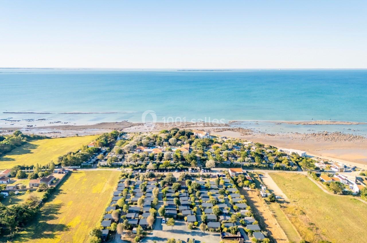 Vue aérienne d'un village côtier entouré de champs, avec une plage et l'océan en arrière-plan.
