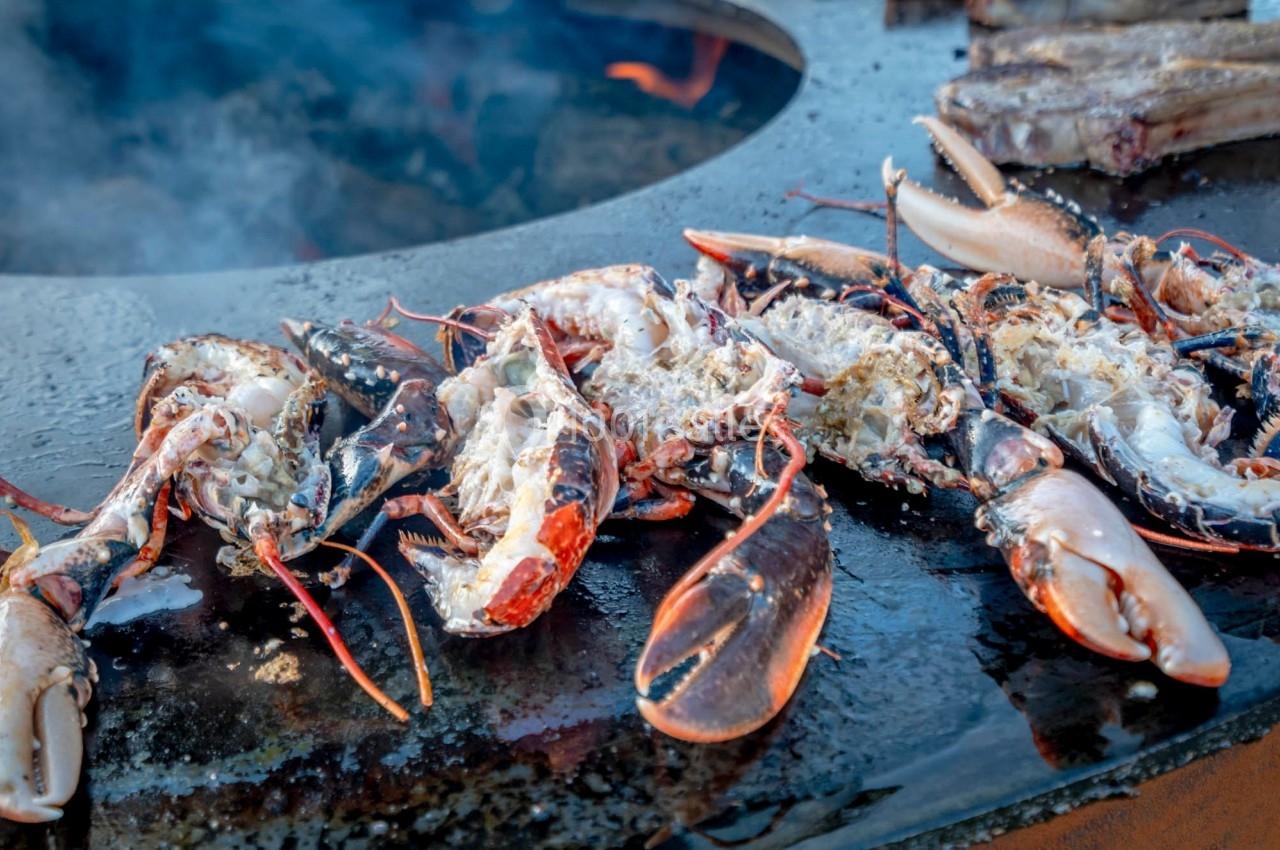 Homards grillés ouverts en deux, cuisant sur une plaque chauffante en extérieur.