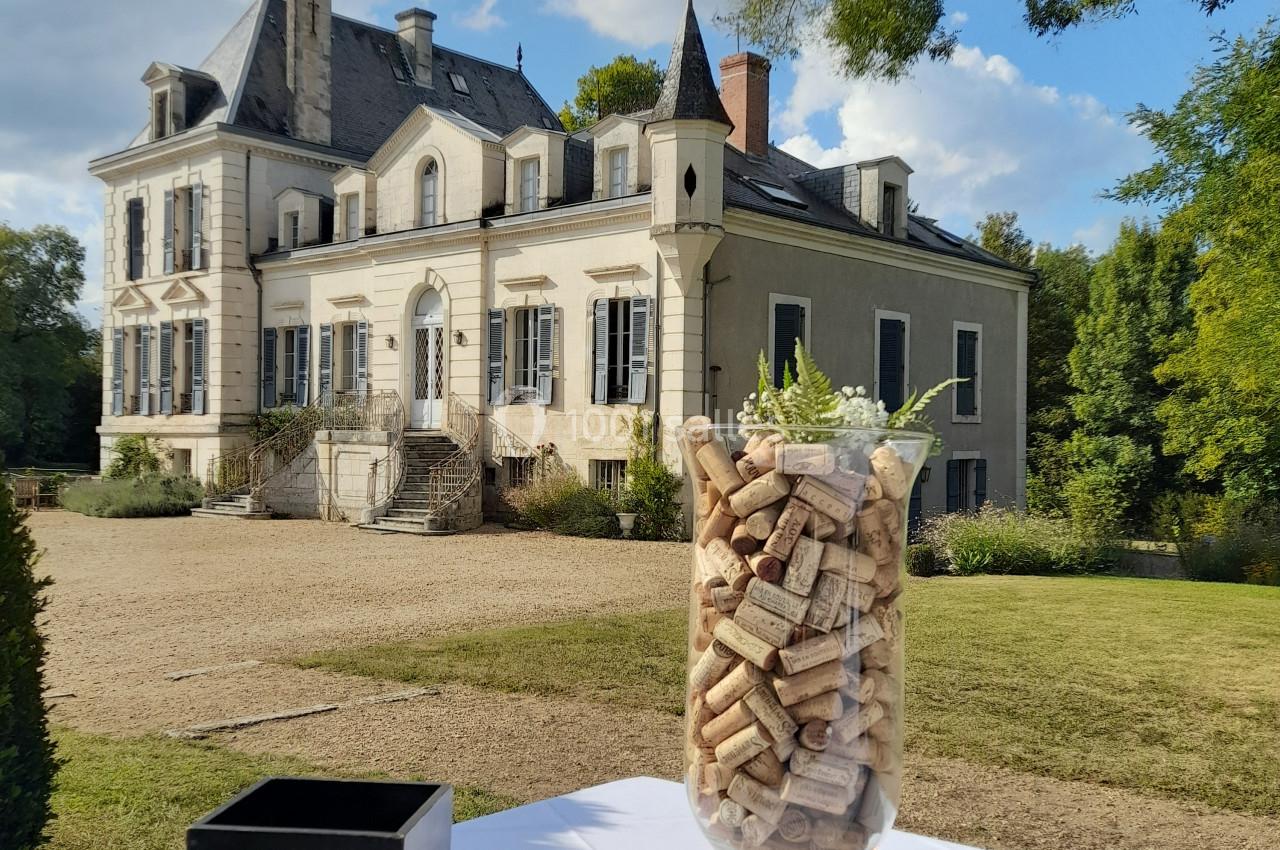 Un grand vase rempli de bouchons en liège posé sur une table blanche devant un château sous un ciel nuageux.