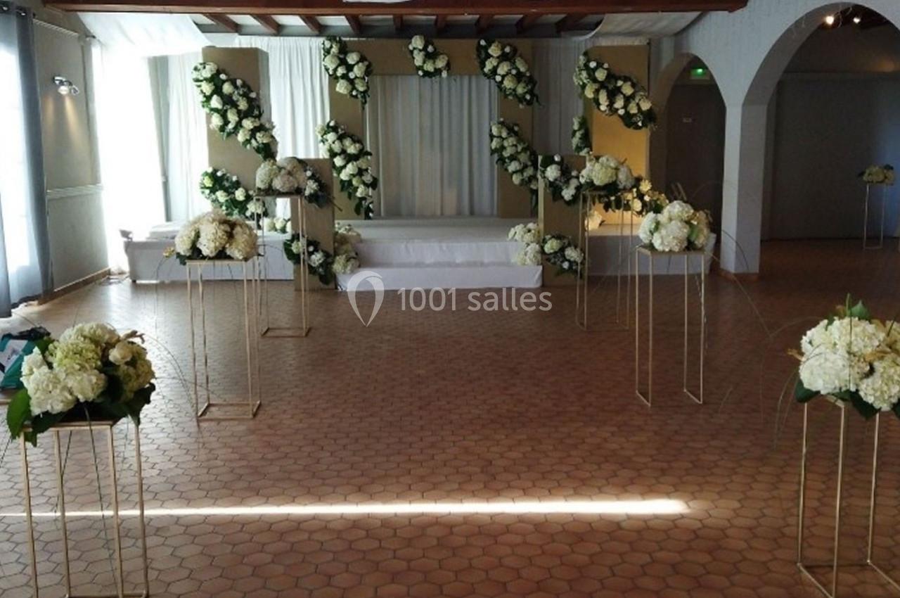 Salle décorée pour un événement avec des arrangements floraux blancs sur des supports dorés et une estrade en arrière-plan.