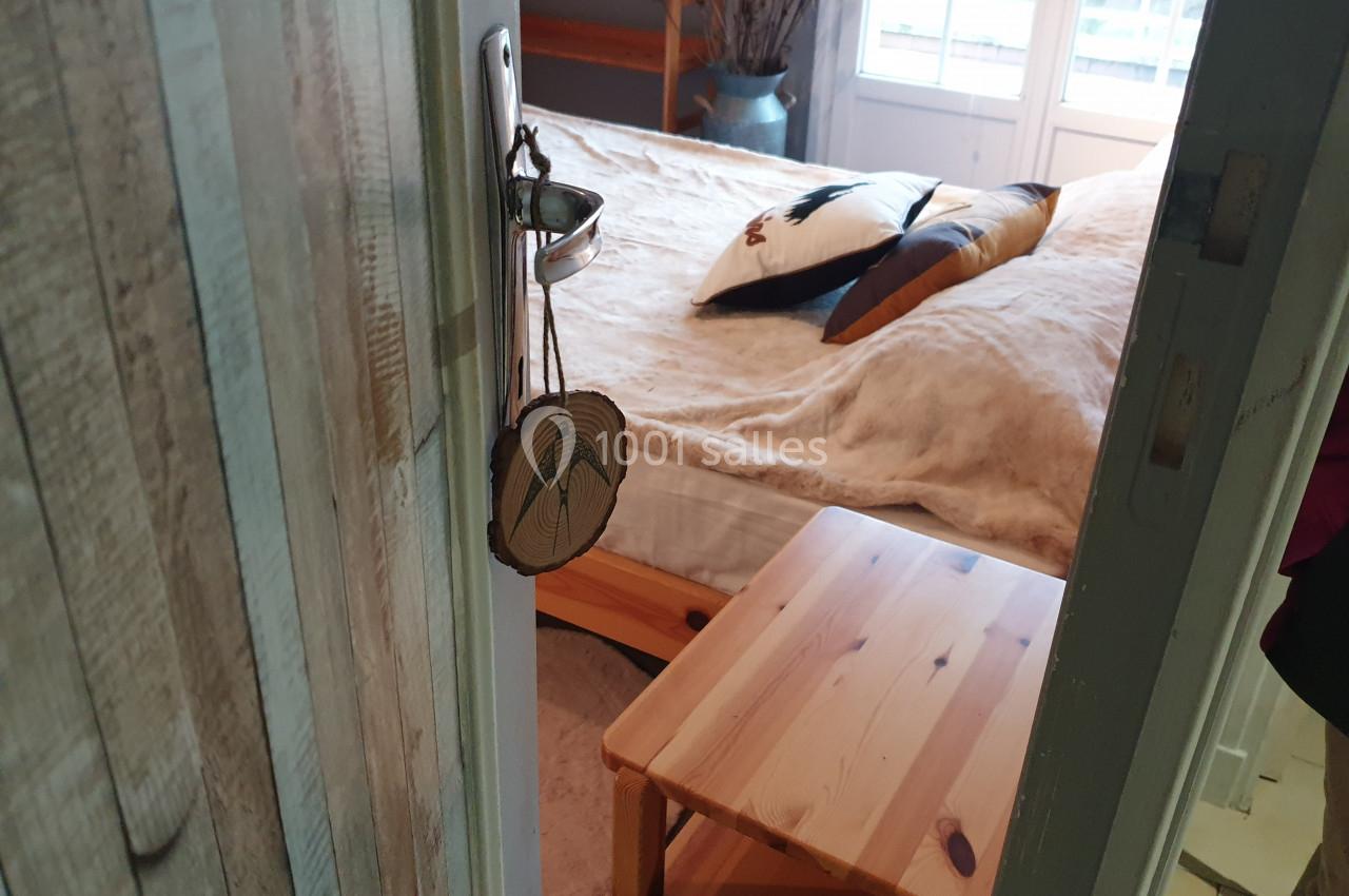 Vue d'une chambre avec un lit double, une table en bois et une fenêtre laissant entrer la lumière naturelle.