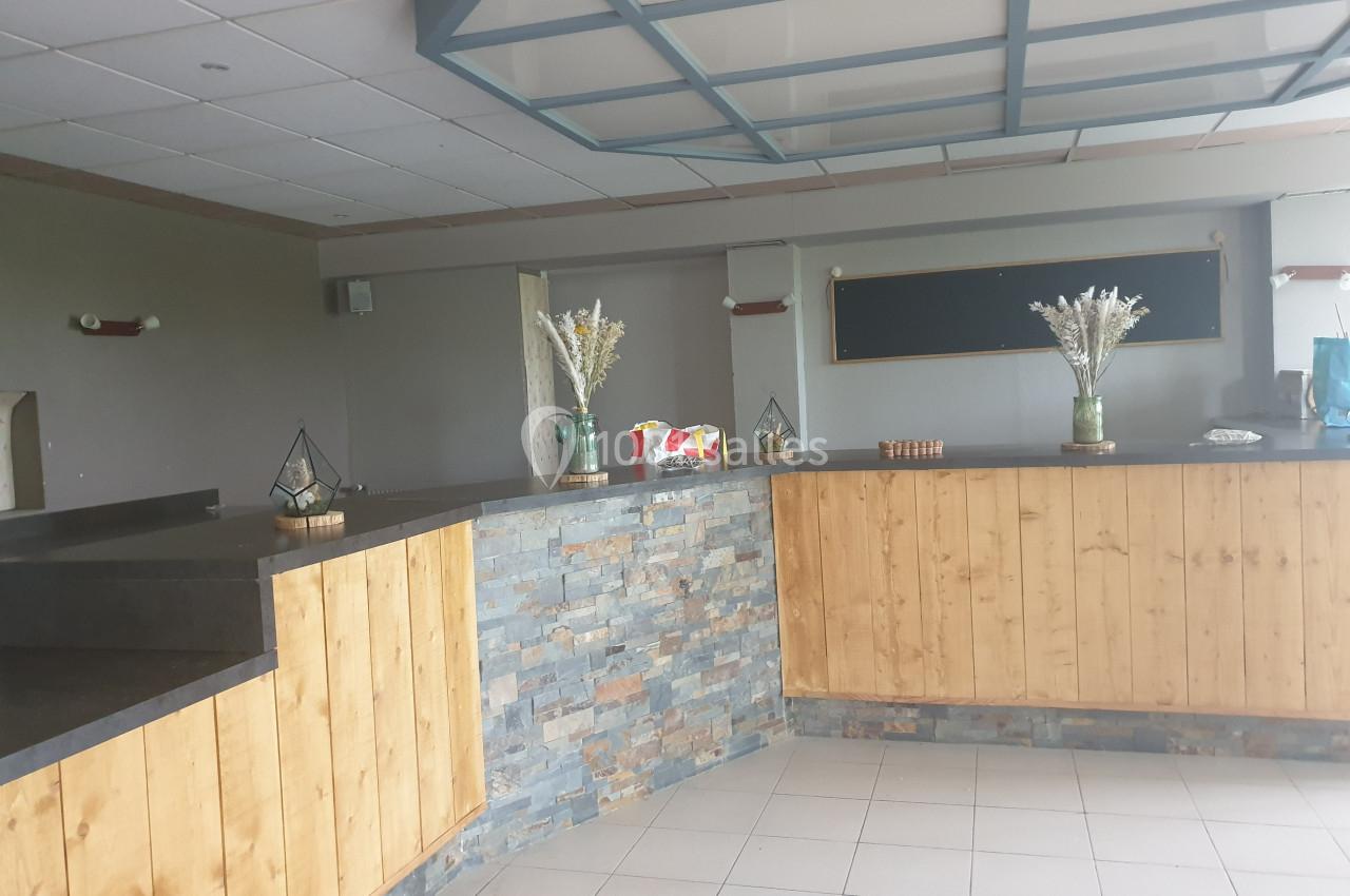 Comptoir en bois et pierre dans une salle avec décoration sobre, vases fleuris et tableau noir au mur.