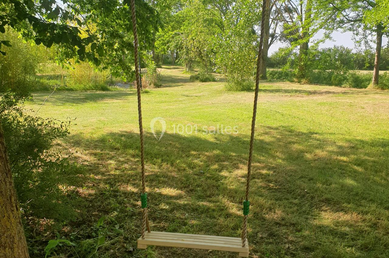 Balançoire en bois suspendue à des cordes, installée entre des arbres dans un jardin verdoyant.