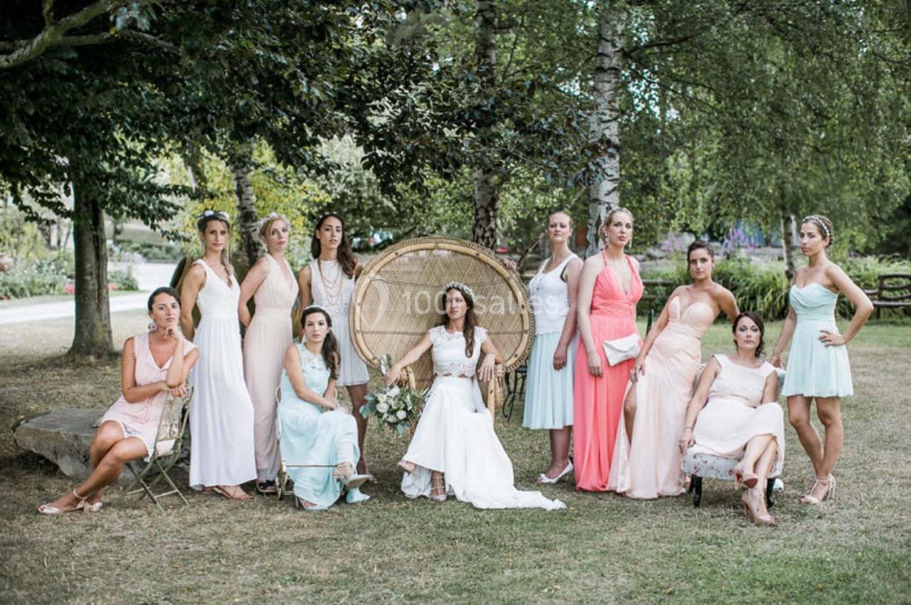 Une mariée en robe blanche entourée de demoiselles d'honneur en robes pastel dans un jardin verdoyant.