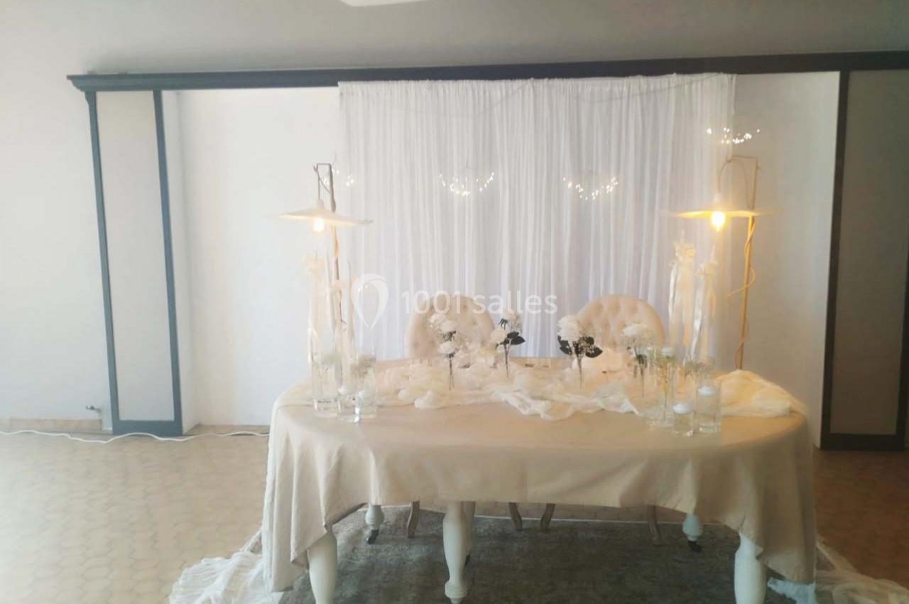 Table décorée pour un événement avec nappes beiges, chaises capitonnées, fleurs blanches et éclairage doux.