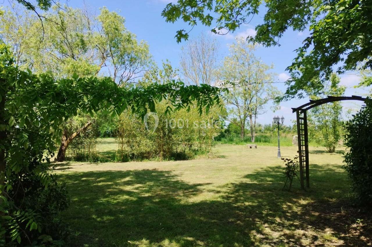 Jardin verdoyant avec pelouse, arbres et arche en bois sous un ciel bleu dégagé.