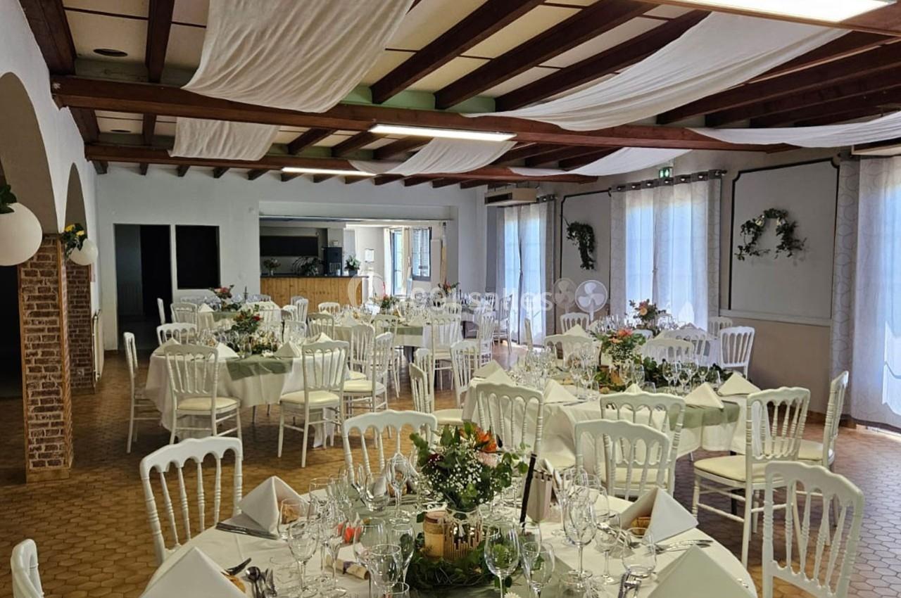 Salle de réception décorée avec des tables dressées, nappes blanches, chaises élégantes et arrangements floraux.