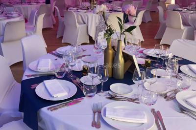 Table ronde élégamment dressée avec nappes blanches, assiettes, couverts, verres et serviettes ornées d'anneaux dorés.