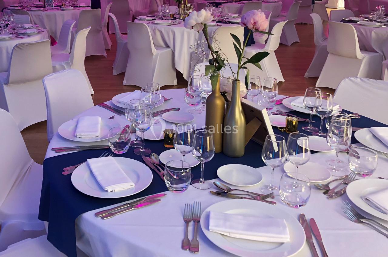 Salle de réception avec tables rondes dressées, nappes blanches et décorations florales élégantes.