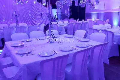 Table ronde élégamment dressée avec nappes blanches, assiettes, couverts, verres et serviettes ornées d'anneaux dorés.