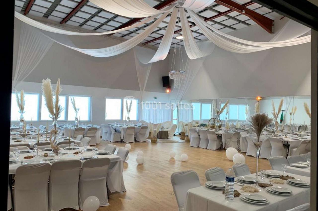 Salle de réception décorée avec des nappes blanches, des tables dressées et des drapés suspendus au plafond.