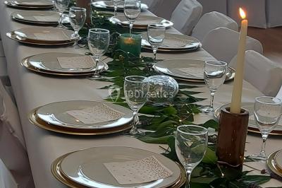 Table ronde élégamment dressée avec nappes blanches, assiettes, couverts, verres et serviettes ornées d'anneaux dorés.