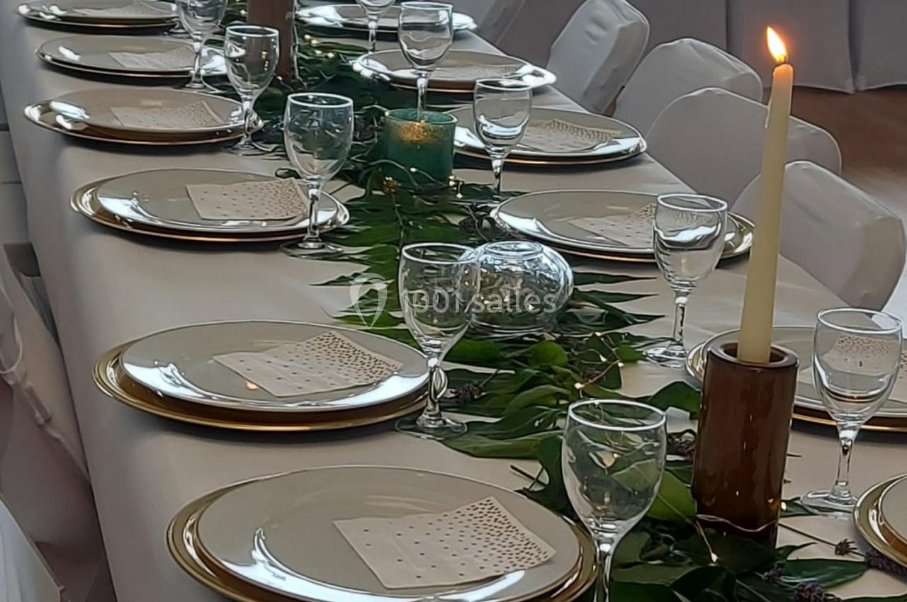 Table décorée pour un événement, avec vaisselle élégante, bougies allumées et feuillage en centre de table.