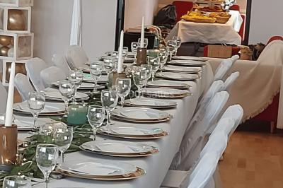 Table ronde élégamment dressée avec nappes blanches, assiettes, couverts, verres et serviettes ornées d'anneaux dorés.