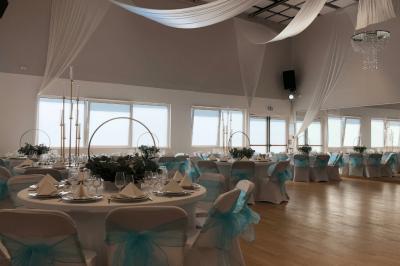 Table ronde élégamment dressée avec nappes blanches, assiettes, couverts, verres et serviettes ornées d'anneaux dorés.