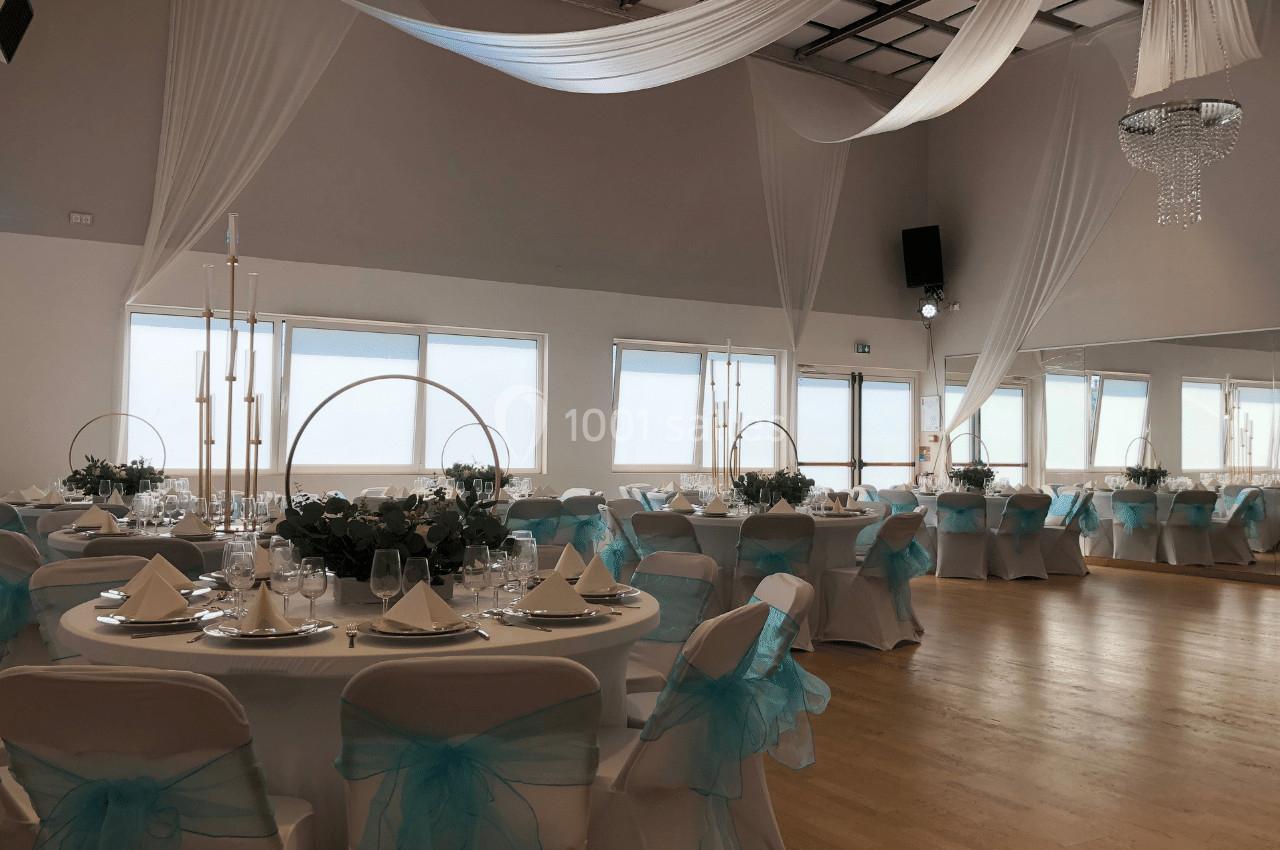 Salle de réception décorée avec des nappes blanches, des chaises ornées de nœuds bleus et des tables élégamment dressées.