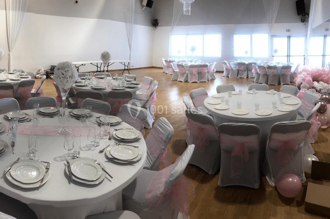 Salle de réception décorée avec des nappes blanches, des chaises ornées de nœuds roses et des tables dressées.