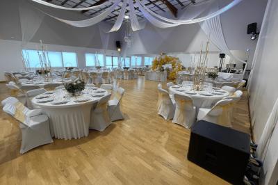 Table ronde élégamment dressée avec nappes blanches, assiettes, couverts, verres et serviettes ornées d'anneaux dorés.