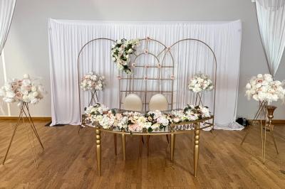 Table ronde élégamment dressée avec nappes blanches, assiettes, couverts, verres et serviettes ornées d'anneaux dorés.