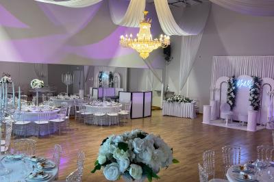 Table ronde élégamment dressée avec nappes blanches, assiettes, couverts, verres et serviettes ornées d'anneaux dorés.