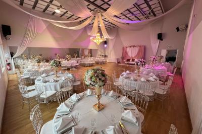 Table ronde élégamment dressée avec nappes blanches, assiettes, couverts, verres et serviettes ornées d'anneaux dorés.