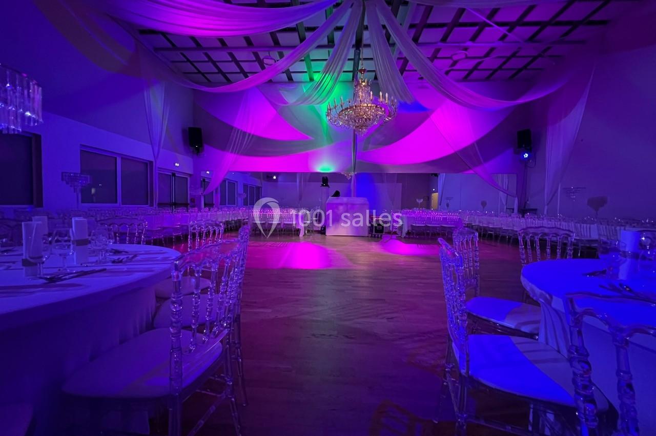 Salle de réception décorée avec des drapés suspendus, des chaises transparentes et un éclairage coloré.