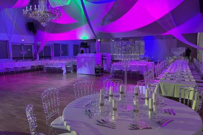 Table ronde élégamment dressée avec nappes blanches, assiettes, couverts, verres et serviettes ornées d'anneaux dorés.