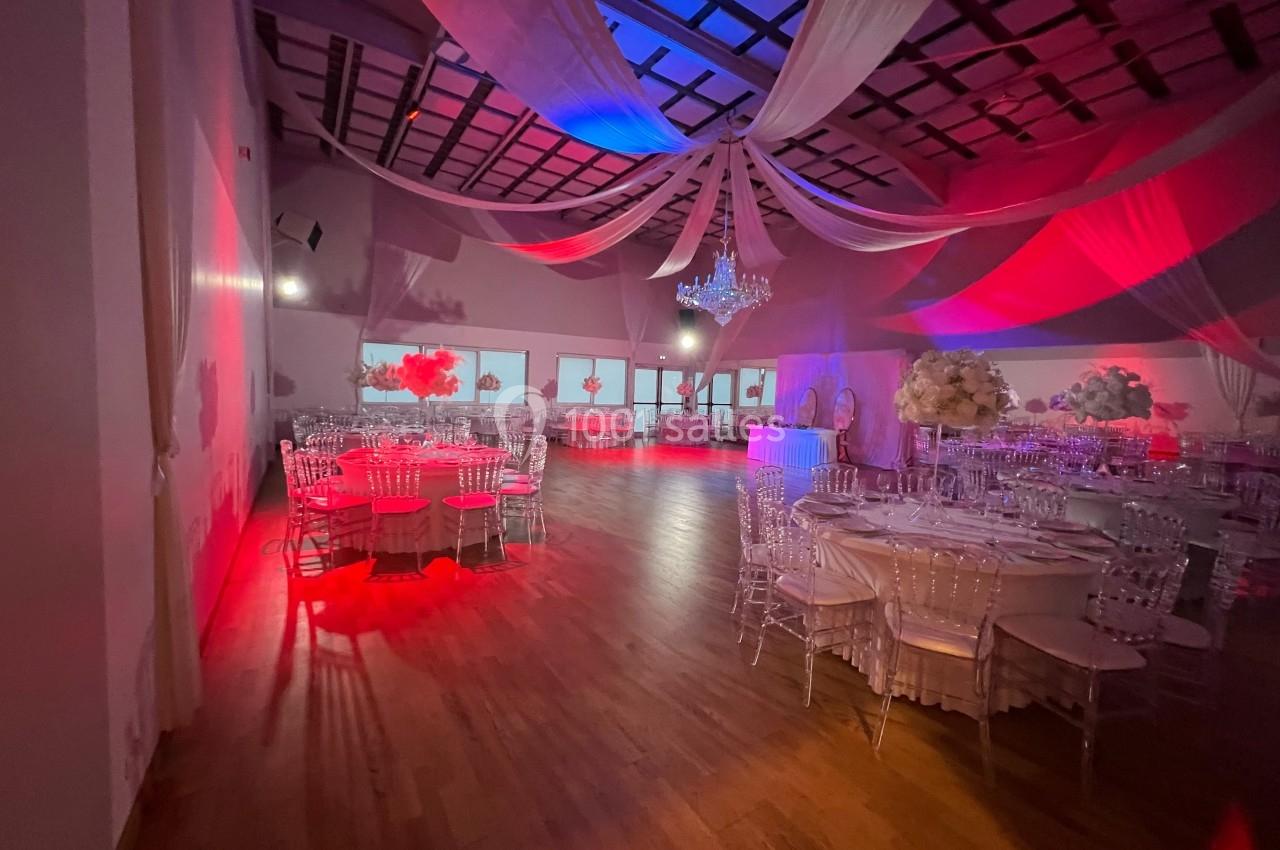 Salle de réception décorée avec des tables rondes, des chaises transparentes, un éclairage rouge et un lustre central.