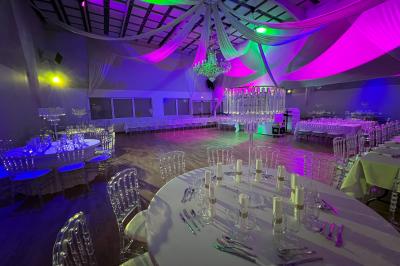 Table ronde élégamment dressée avec nappes blanches, assiettes, couverts, verres et serviettes ornées d'anneaux dorés.