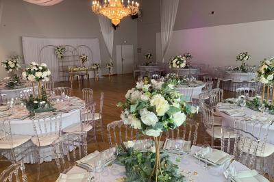 Table ronde élégamment dressée avec nappes blanches, assiettes, couverts, verres et serviettes ornées d'anneaux dorés.