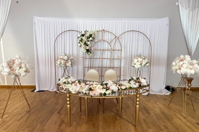Table ronde élégamment dressée avec nappes blanches, assiettes, couverts, verres et serviettes ornées d'anneaux dorés.