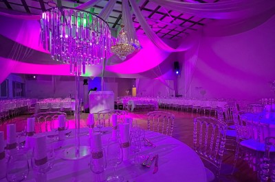 Table ronde élégamment dressée avec nappes blanches, assiettes, couverts, verres et serviettes ornées d'anneaux dorés.