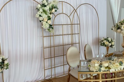 Table ronde élégamment dressée avec nappes blanches, assiettes, couverts, verres et serviettes ornées d'anneaux dorés.