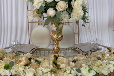 Table ronde élégamment dressée avec nappes blanches, assiettes, couverts, verres et serviettes ornées d'anneaux dorés.