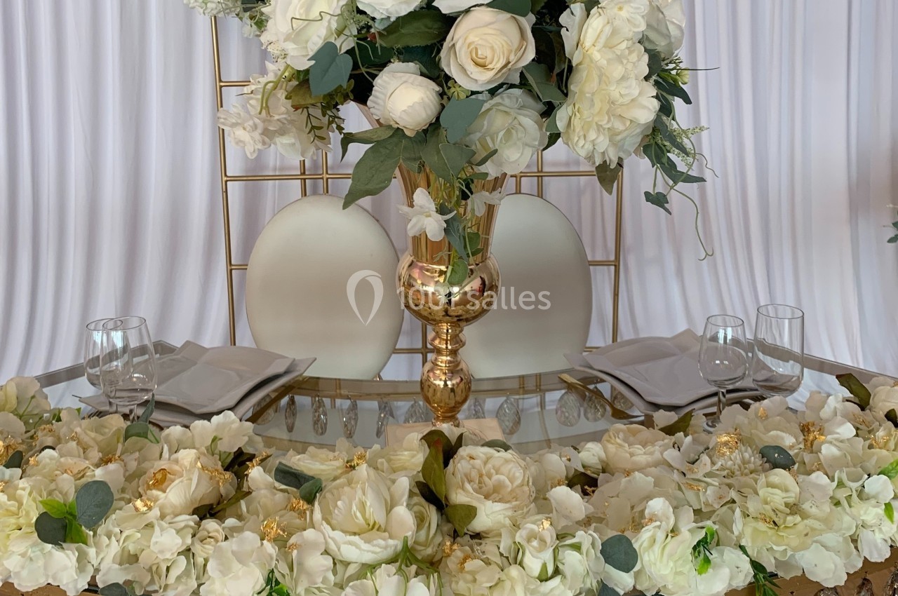 Décoration de table élégante avec des fleurs blanches, un vase doré et deux assiettes disposées sur une nappe blanche.