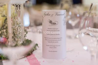 Centre de table avec bouquet de fleurs blanches et roses, numéro de table ’1’ et bougies sur une nappe blanche.
